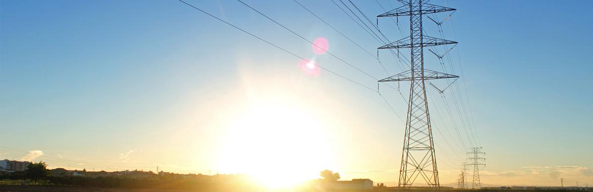 A bright sun shining in a blue sky over a field with electricity pylons 